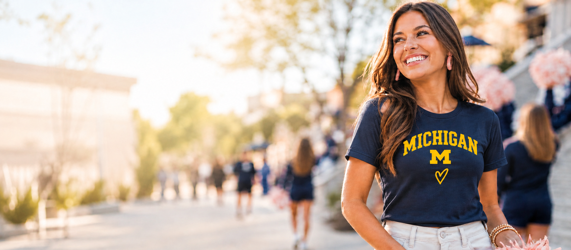 Smiling Michigan fan in a navy MICHIGAN tee with a maize block M, on a sunlit campus walkway